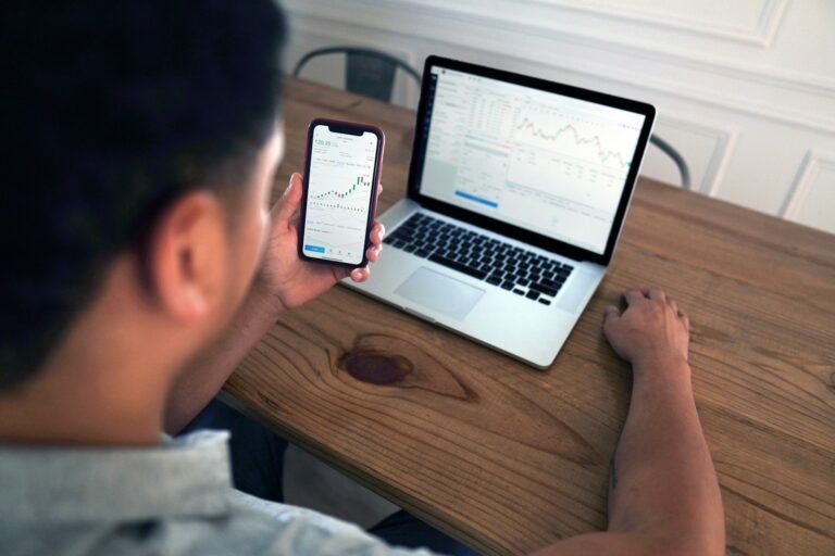 Osoba sleduje grafy na mobilním telefonu, zatímco má na stole notebook. Ideální řešení pro práci i sledování trhu díky stabilnímu připojení, které poskytuje Starlink.