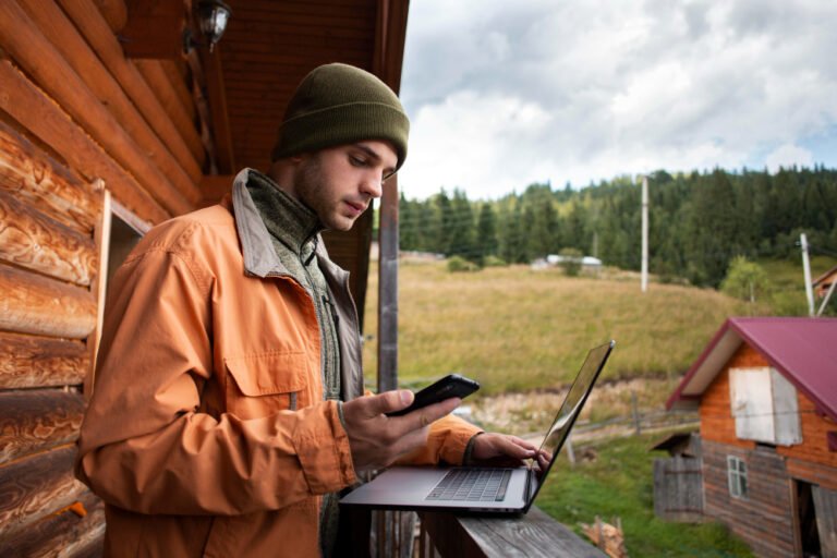 Muž na venkovské chatě pracující na notebooku a telefonu díky připojení Starlink internetu.
